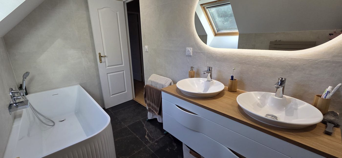 Salle de bain après rénovation : double vasque, carrelage beige et baignoire îlot