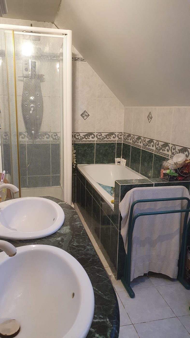 Salle de bain avant travaux : carrelage vert, baignoire encastrée et cabine de douche